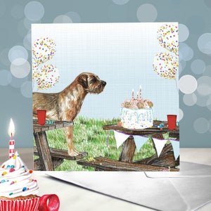 May include: A brown and white dog sits at a picnic table with a birthday cake and balloons. The cake is decorated with sprinkles and candles. The dog is looking at the cake.