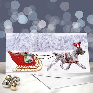 May include: A Christmas card depicting a dog with antlers pulling a red sleigh laden with presents. The background shows a snow-covered forest. The rectangular card has a white envelope and gold and silver bells.