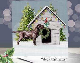 May include: A Christmas card featuring a brown Labrador Retriever standing in front of a dog house decorated with lights and a wreath. The dog house has a bone-shaped sign and mistletoe. The text "deck the halls" is at the bottom.