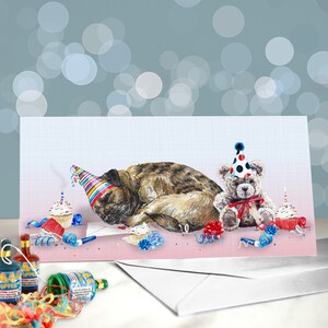 May include: A birthday card featuring a brown and black dog wearing a colorful party hat, sleeping next to a teddy bear wearing a blue and white party hat. The card is decorated with confetti, party horns, and cupcakes.