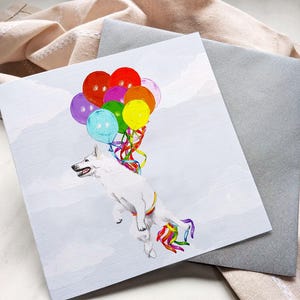 May include: A square greeting card featuring a white dog floating in the air, held up by a cluster of colorful balloons in red, orange, yellow, green, blue, and purple. The dog has a rainbow-colored harness and a matching rainbow tail decoration.