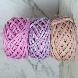 May include: Three balls of yarn in pink, purple and beige colours. The yarn is thick and chunky, perfect for crocheting or knitting.