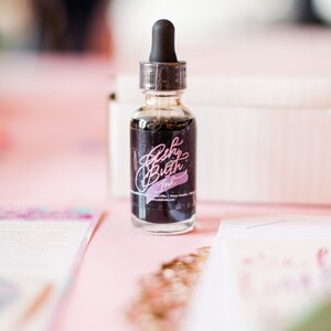 May include: A small glass bottle of black ink with a dropper top. The bottle has a label that says "Brush Lettering Ink" in pink lettering.