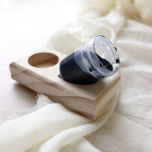 May include: A wooden dye holder with two compartments, one containing a small plastic cup filled with dark blue dye.