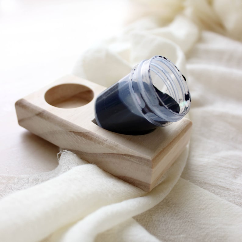 May include: A wooden dye holder with two compartments, one containing a small plastic cup filled with dark blue dye.