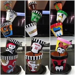 Pode incluir: Um conjunto de três vasos de flores empilhados, cada um decorado com um design diferente. O vaso superior apresenta uma imagem de desenho animado do Mickey Mouse, o vaso do meio tem uma camisa de futebol com o texto "Montana 16", e o vaso inferior tem um logotipo dos San Francisco 49ers.