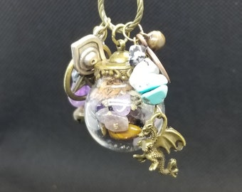 May include: A gold chain necklace with a glass bottle pendant filled with various crystals and a small gold dragon charm.