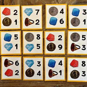 May include: Nine yellow cards with numbers and images. Each card has a different combination of a red gem, a blue gem, a coin, a ring, and a number. The numbers range from 1 to 9.