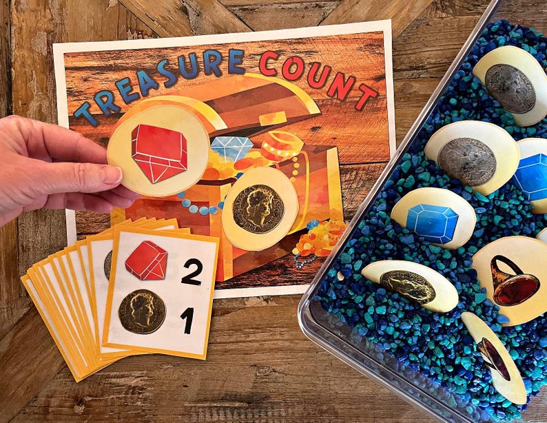 May include: A colorful learning game for kids featuring a treasure chest with gems and coins. The game includes a set of cards with numbers and images of red gems and gold coins. The game is designed to help children learn to count.