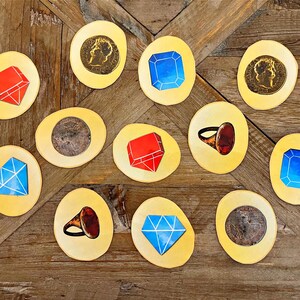 May include: Twelve yellow circular game pieces with various images, including red and blue gems, a gold ring with a red stone, and gold coins.