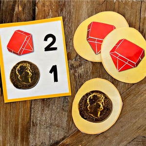 May include: A yellow card with the numbers 2 and 1 printed on it. There are two red gems and two gold coins on the card. The gems and coins are also on separate yellow circles.