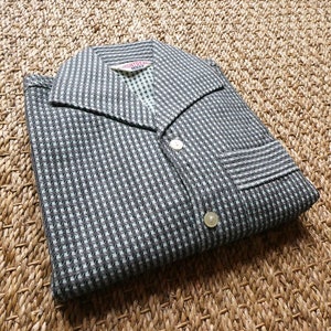 May include: A black and white checkered shirt with a collar and button closure. The shirt has a pocket on the left side and a label that reads "MONTY HALL".