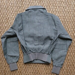 May include: A gray and white checkered jacket with a button-up collar and long sleeves. The jacket has a ribbed waistband and cuffs.