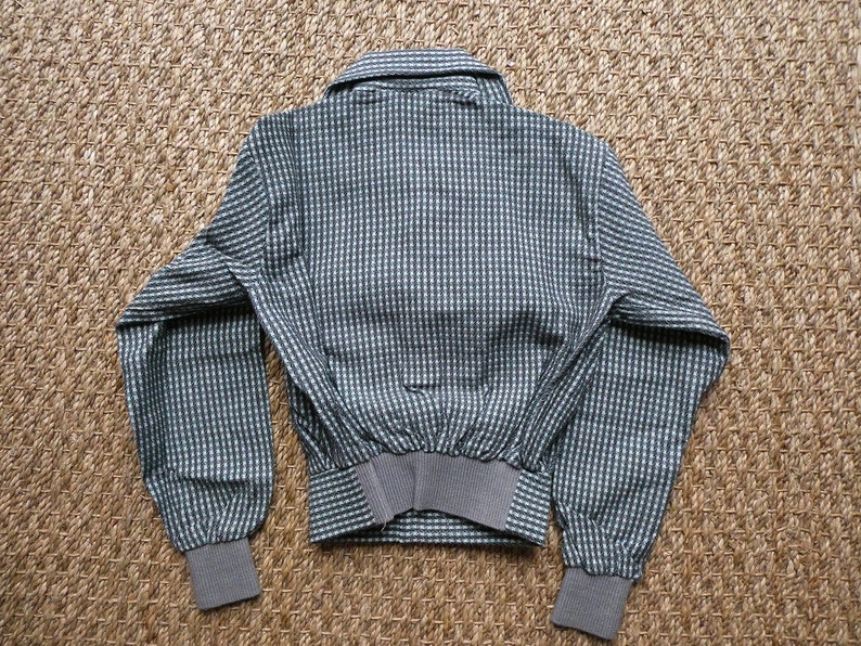 May include: A gray and white checkered jacket with a button-up collar and long sleeves. The jacket has a ribbed waistband and cuffs.