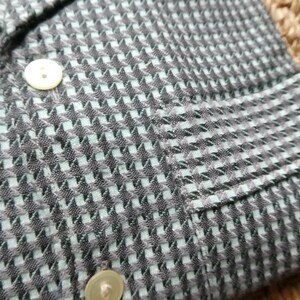 May include: A close-up of a black and light blue patterned shirt with a pocket on the left side. The shirt has a button closure and a collar.