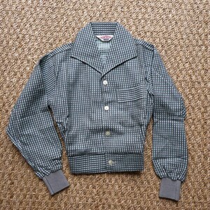 May include: A gray and white checkered button-up shirt with a collar and long sleeves. The shirt has a pocket on the left side and a label that reads "MONTY'S" on the inside of the collar.