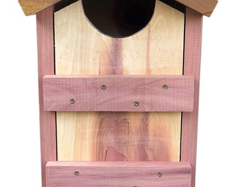 Könnte beinhalten: Ein Vogelhaus aus Holz mit einer Fassade aus Zedernholz und einem Dach aus braunem Zedernholz. Das Vogelhaus hat eine Flügeltür mit einem Riegel und zwei Holzregale im Inneren.