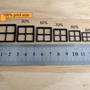May include: A ruler with centimetre markings next to six black square window frame models of varying sizes, labelled from 50% to 100% print size. The text "100% print size" is in a yellow box.