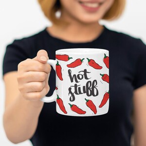 May include: White ceramic mug with a red chili pepper pattern and the text "hot stuff" in black.