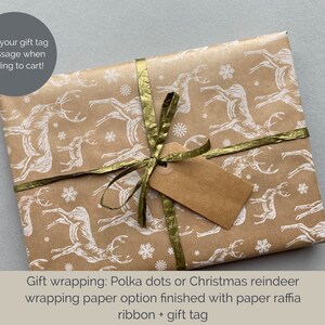 May include: A brown gift box wrapped in paper with a white reindeer pattern. The box is tied with a gold ribbon and a brown gift tag.