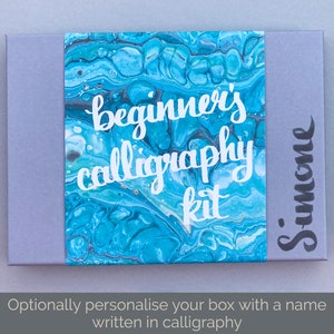 May include: A gray box with a blue and white marbled design. The box has the text "beginner's calligraphy kit" in white lettering. The box is labeled "Simone" in black calligraphy.