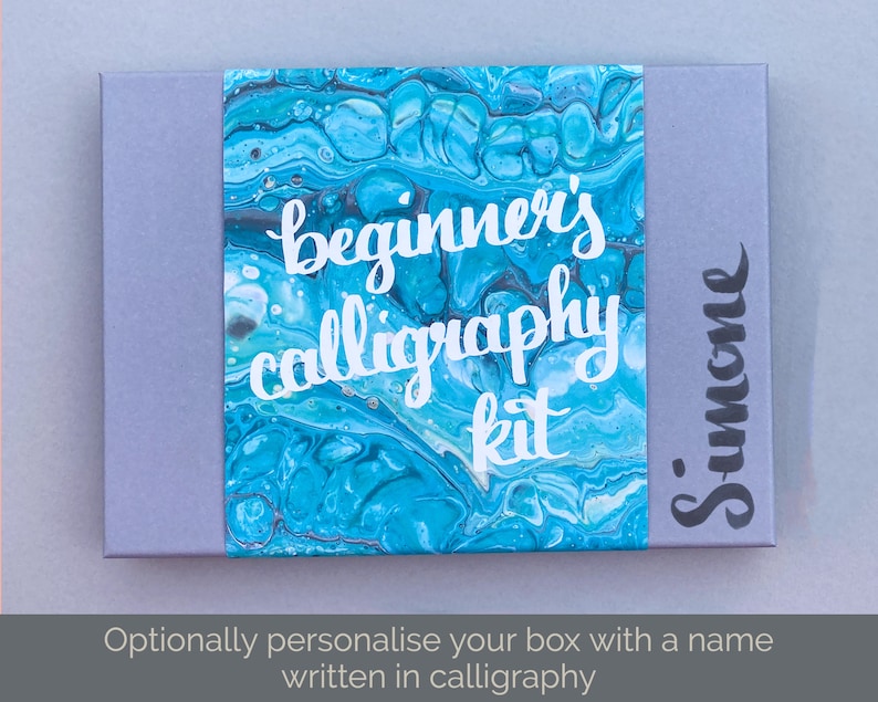 May include: A gray box with a blue and white marbled design. The box has the text "beginner's calligraphy kit" in white lettering. The box is labeled "Simone" in black calligraphy.