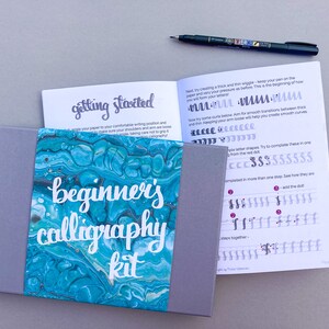 May include: A beginner's calligraphy kit with a gray box and a blue and green marbled design. The box contains a booklet with the title "getting started" and "beginner's calligraphy kit".