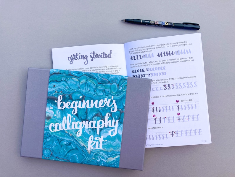 May include: A beginner's calligraphy kit with a gray box and a blue and green marbled design. The box contains a booklet with the title "getting started" and "beginner's calligraphy kit".