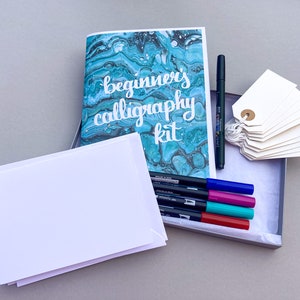 May include: A calligraphy kit with a blue and white marbled cover that says "beginner's calligraphy kit". The kit includes a set of colored markers, blank cards, and tags.
