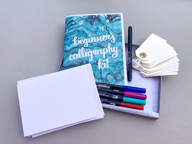 May include: A calligraphy kit with a blue and white marbled cover that says "beginner's calligraphy kit". The kit includes a set of colored markers, blank cards, and tags.
