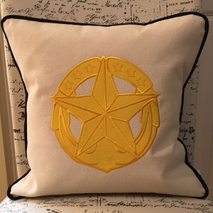 May include: A white throw pillow with a black border and a gold embroidered five-pointed star with a circle of smaller stars around it.