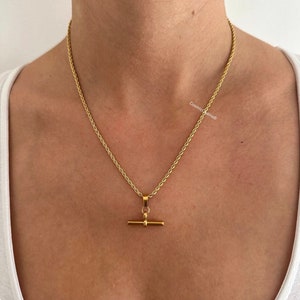 May include: A gold rope chain necklace with a gold t-bar pendant.