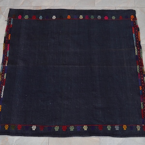 May include: A dark blue rug with a colorful geometric border. The rug has a simple design and is made of a soft, woven material.
