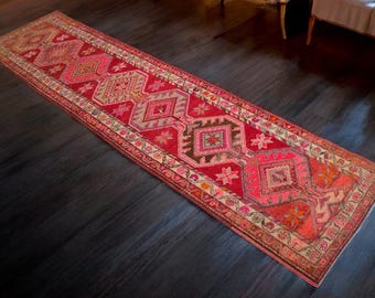 Puede incluir: Una alfombra de pasillo larga y estrecha con un diseño persa tradicional. La alfombra es predominantemente roja con intrincados patrones en tonos de rosa, naranja y marrón. La alfombra tiene un borde con flecos.