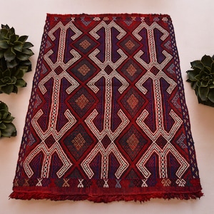 May include: A red, blue, and white patterned rug with a geometric design. The rug has a fringe border.