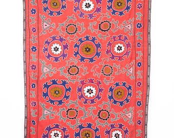 May include: A red fabric wall hanging with a repeating pattern of embroidered flowers and geometric shapes in shades of blue, white, brown, and pink. The fabric has a fringe border and the text "1936 10/X" is visible in the bottom right corner.
