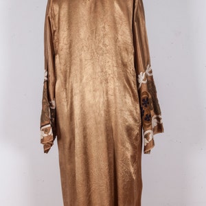 May include: A long, gold-colored robe with embroidered floral details on the sleeves. The robe is made of a silky fabric and has a simple, elegant design.