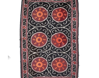 May include: A black and white textile with a repeating pattern of red and orange circles. The circles are surrounded by a swirling design. The textile has a border of small red and orange circles.