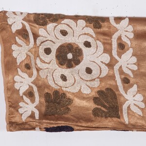May include: A brown velvet fabric with white and brown embroidery. The embroidery features a floral design with a central circle and surrounding petals.