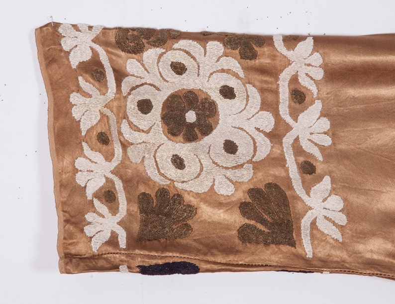 May include: A brown velvet fabric with white and brown embroidery. The embroidery features a floral design with a central circle and surrounding petals.