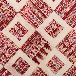 May include: A white fabric with a red, white, and blue embroidered pattern. The pattern is made up of squares and rectangles, and it features a variety of floral and geometric designs.