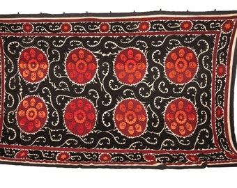 May include: A black fabric wall hanging with a repeating pattern of red and orange floral motifs. The floral motifs are surrounded by a white swirling design.