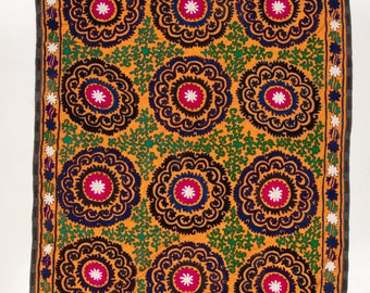 May include: A rectangular embroidered textile with a repeating pattern of circular motifs. The motifs are in shades of black, blue, green, pink, and white on a bright orange background.