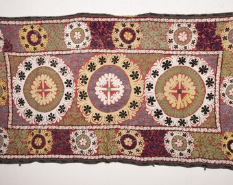 May include: A rectangular embroidered tapestry with a central design of three large, concentric circles with a cross in the center. The circles are surrounded by smaller circles and floral motifs. The tapestry is made of a variety of colors, including red, green, yellow, and black.