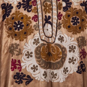 May include: A close-up of a beige fabric with intricate embroidery in shades of brown, white, and black. The embroidery features floral and geometric patterns.