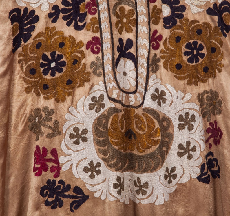 May include: A close-up of a beige fabric with intricate embroidery in shades of brown, white, and black. The embroidery features floral and geometric patterns.