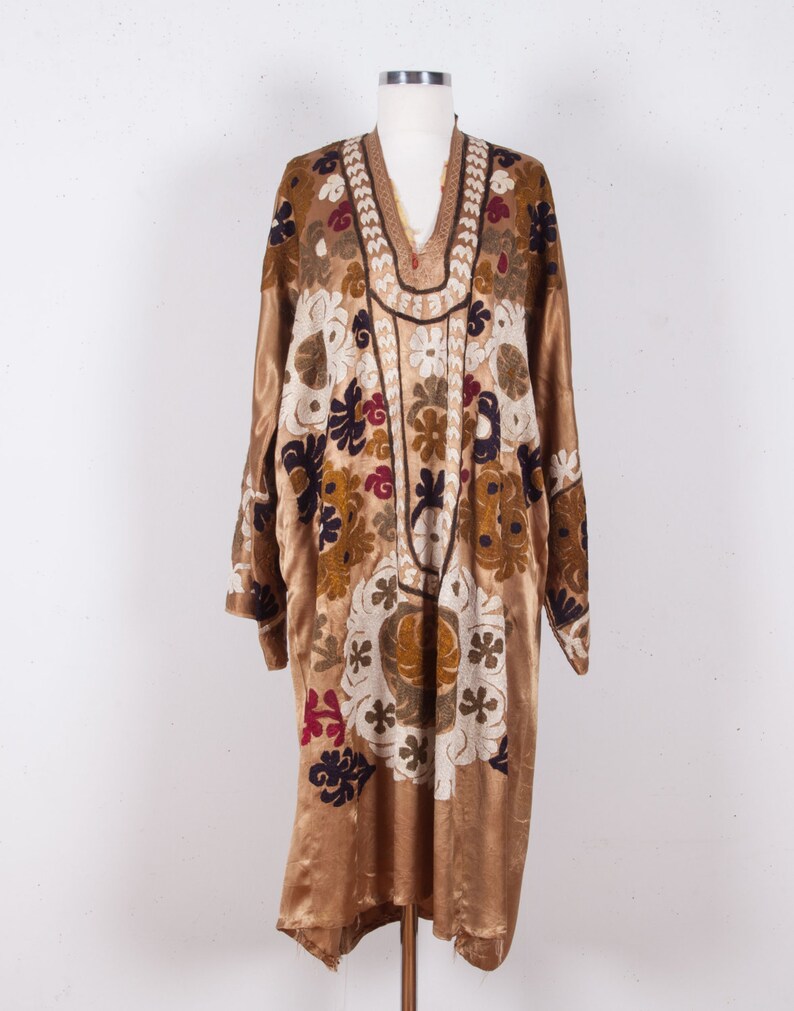 May include: A long, gold-colored robe with a V-neck and intricate floral embroidery in shades of white, brown, red, and blue.