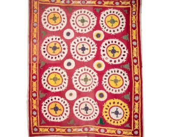May include: A red textile with a repeating pattern of white and yellow circles with a cross in the center. The circles are surrounded by a ring of smaller circles. The textile has a border of yellow and red.