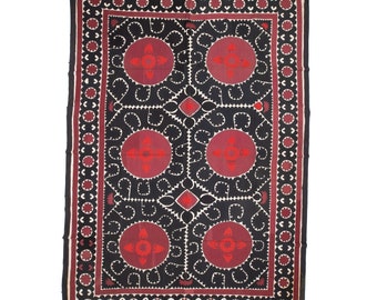 May include: A black and red embroidered textile with a repeating pattern of stylised flowers and leaves. The textile has a border of red and white circles.