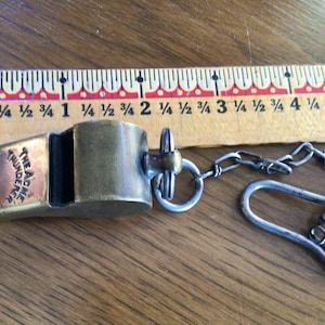May include: A brass whistle with a silver chain attached. The whistle is engraved with the words "The Acme Thunderer".